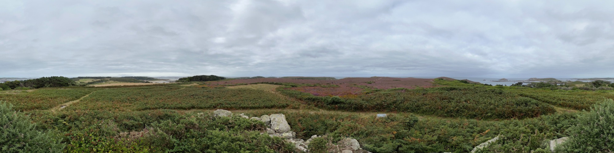 A panoramic view from Beacon Hill on Tresco, Isles of Scilly, showing rolling heathland covered in bracken and heather, with distant views of the sea and nearby islands.