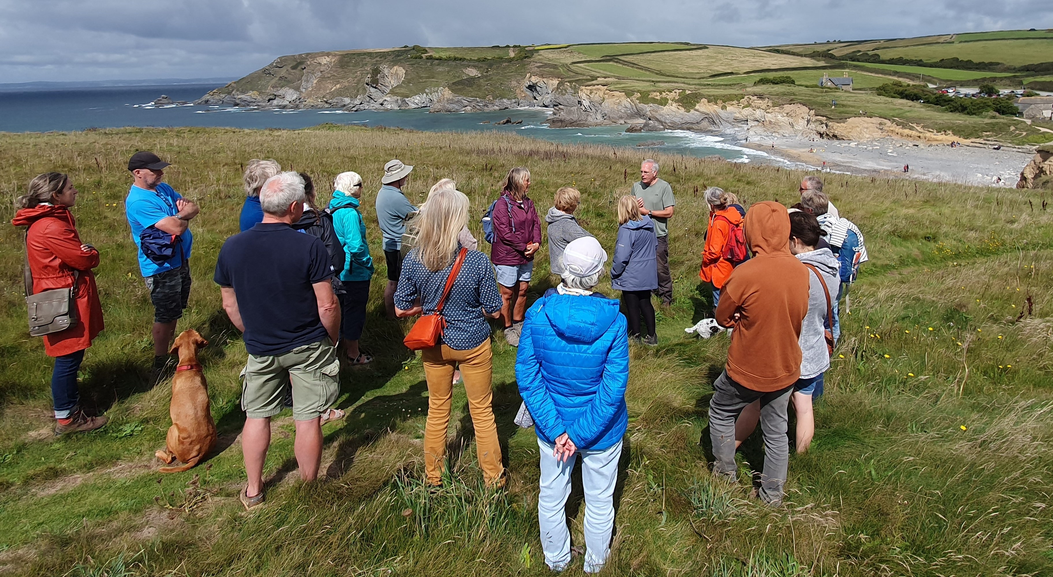 Near the top of the Castle headland, a diver is describing the Schiedam site to the group. People are looking out over Jangye-ryn cove to the site itself, marked by a line of surf off the far end of the beach.