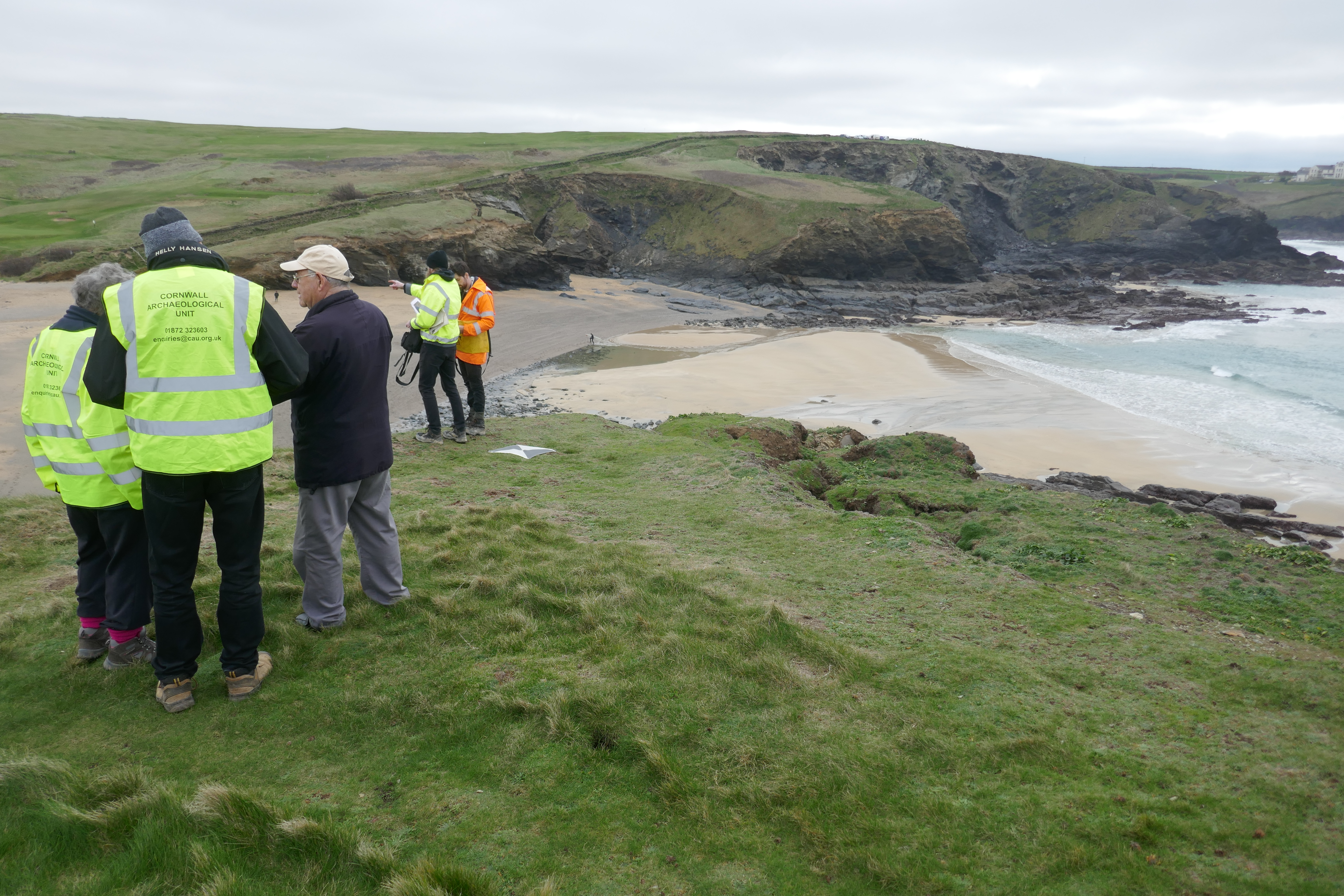 The project team in luminous yellow high visibility vests stand out on the open grassy summit of the headland. The square mark for the drone, quartered in black and white and about the size of a large chessboard, is fixed above the sudden cliff edge. Below is the smooth sand of Church Cove.