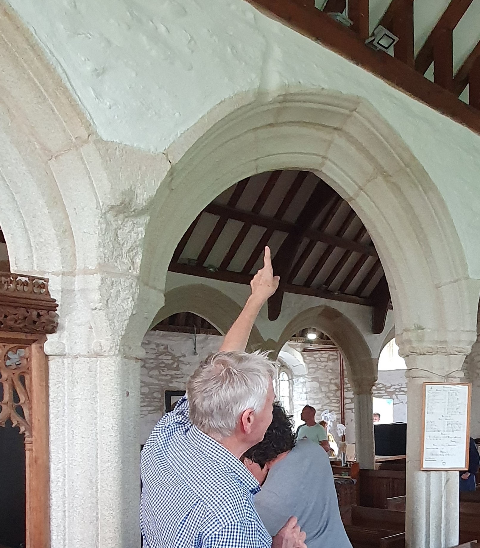 John Allan is pointing up to a cut in the masonry inside the church, high on the north side of the most easterly of the granite pointed arches between the nave and the aisle, on the former line of the screen. The cut, perhaps as long as a forearm, is partly in the head of the arch and partly in the wall above that. It slants out towards the west, as the rood loft did. There is a corresponding rougher cut trimming back the granite at the springing of the same arch.