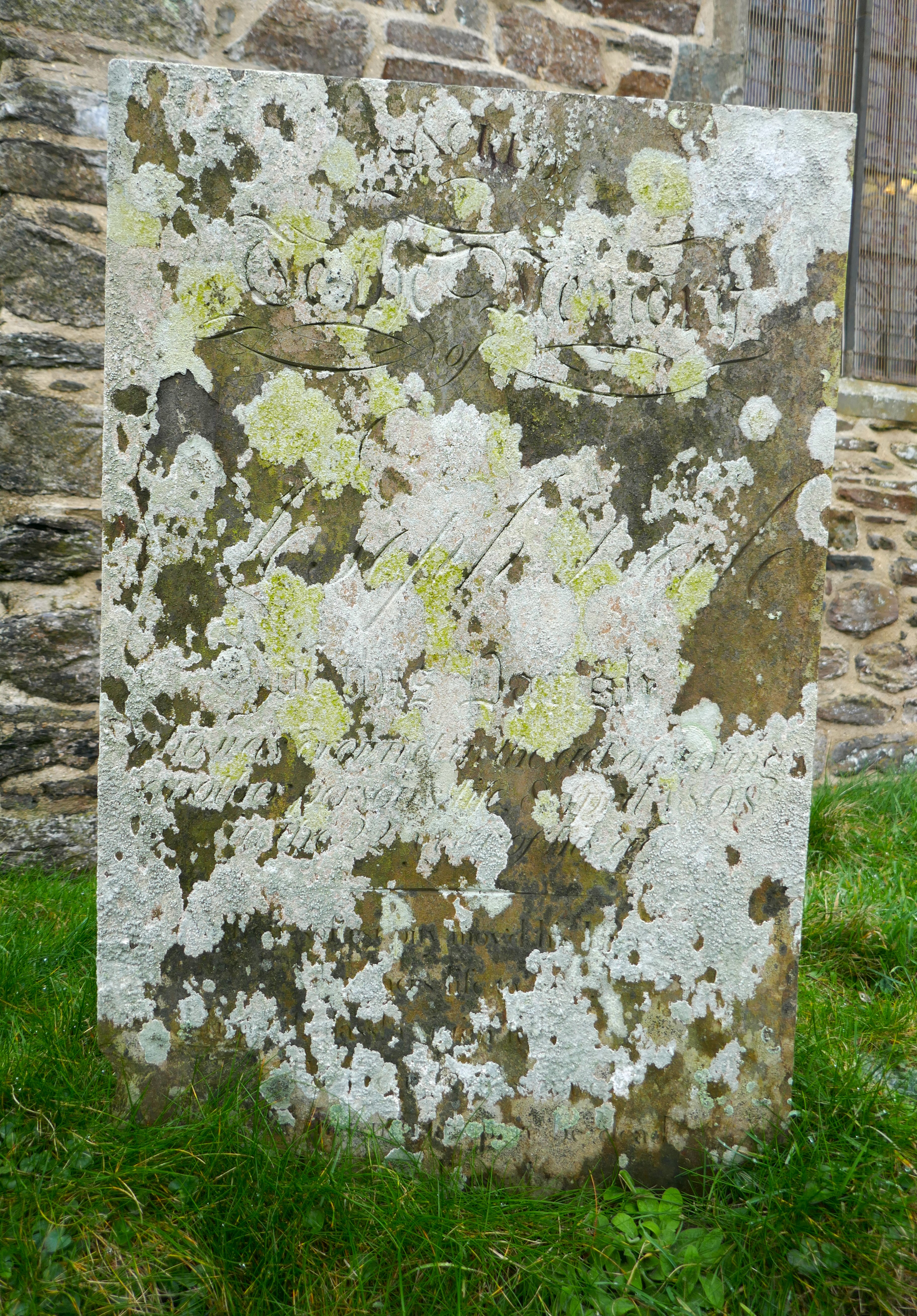 The gravestone is a rectangular slate. It is largely covered by lichen, mostly greyish white, some pale yellow. The name Joseph Dale engraved in elegant flowing script is clearly legible through the lichen. Beneath this the size of the lettering decreases, and it can just be made out with the benefit of the later 19th century transcription.