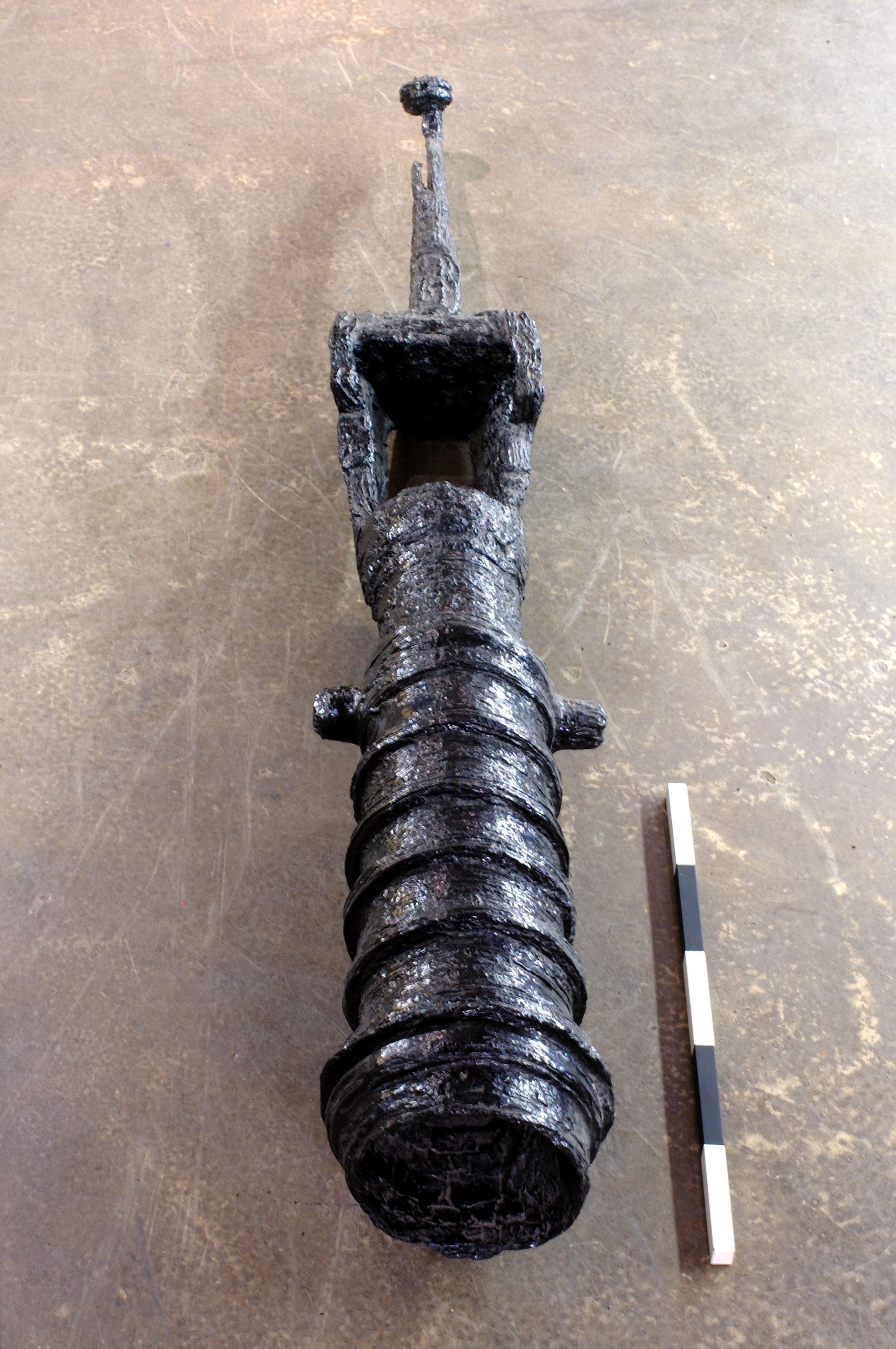 The gun is lying with its ribbed barrel facing towards us and tapering swivel end behind. The iron fabric is rough but appears well-preserved, perhaps newly blacked. A scale indicates it is approximately a metre long.