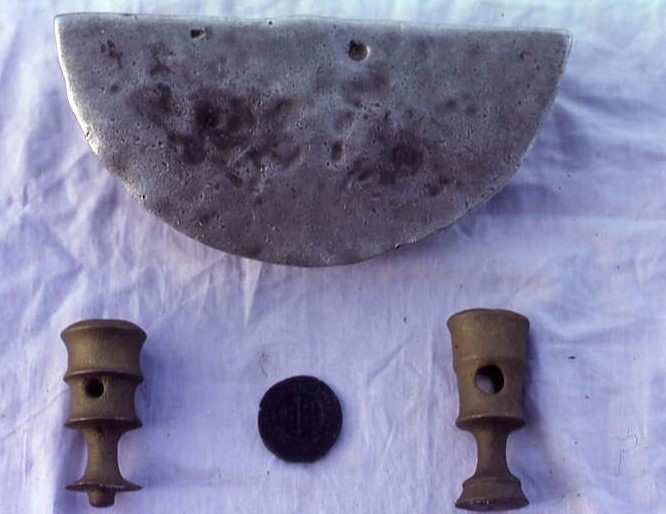 The finds lie on a white sheet in natural light as if spread on the clifftop after landing. They look clean and sharp, especially the half-round ingot with its silver shine.